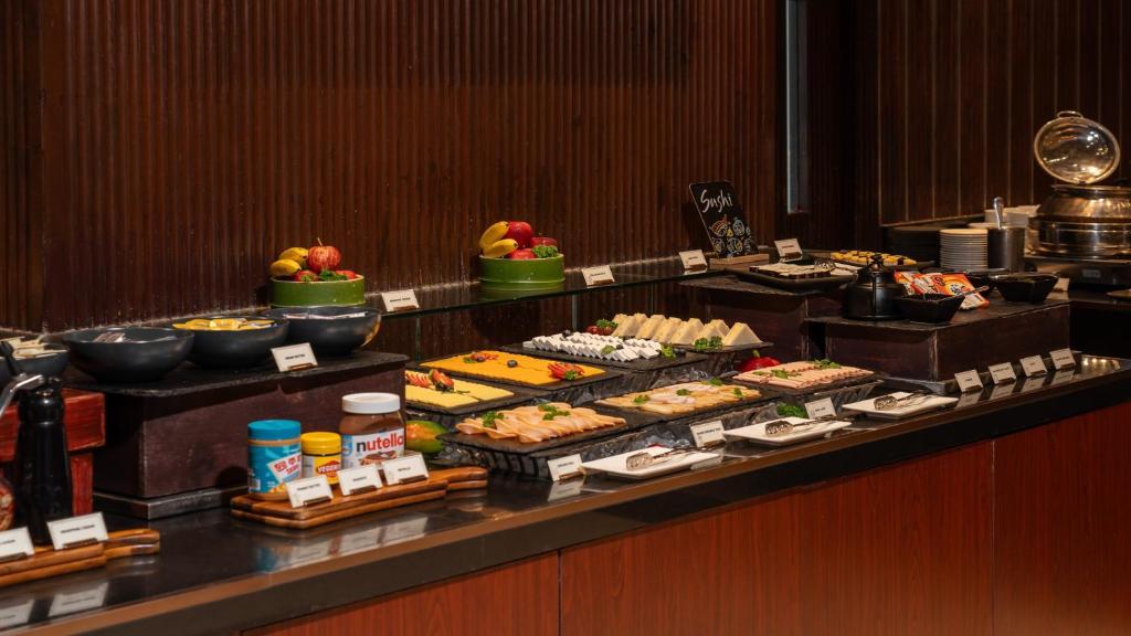 A buffet counter offering fruit, sushi, breads, spreads and hot-food trays.