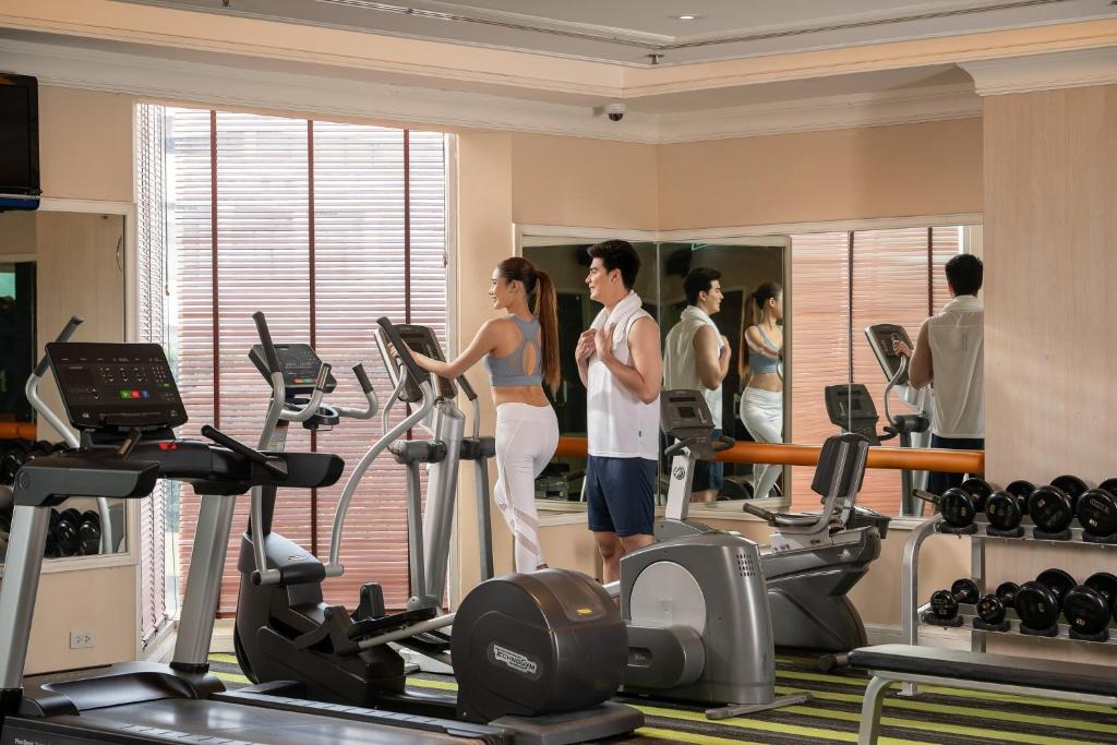 A mirrored fitness room with cardio machines and a dumbbell rack.