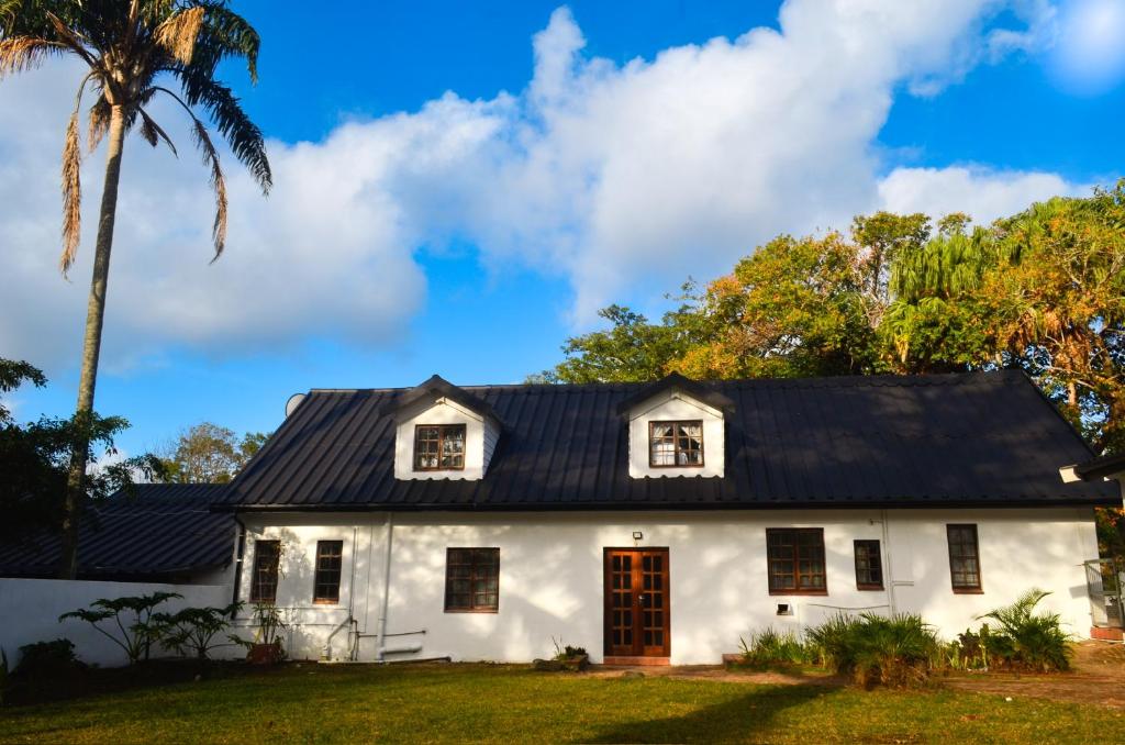 a white house with a black roof and a palm tree at The Meadow Manor in Port Edward