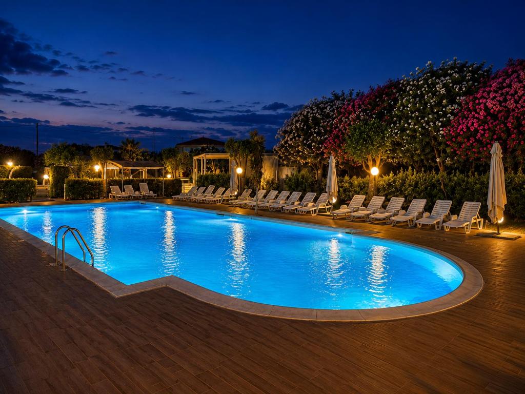 a swimming pool at night with lounge chairs at Hotel Park Village in Rossano