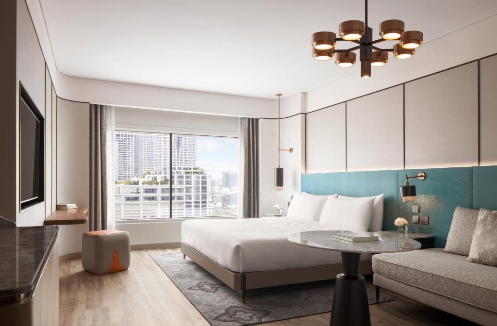 A contemporary bedroom with a large bed, sofa, city-facing window and compact writing surface.