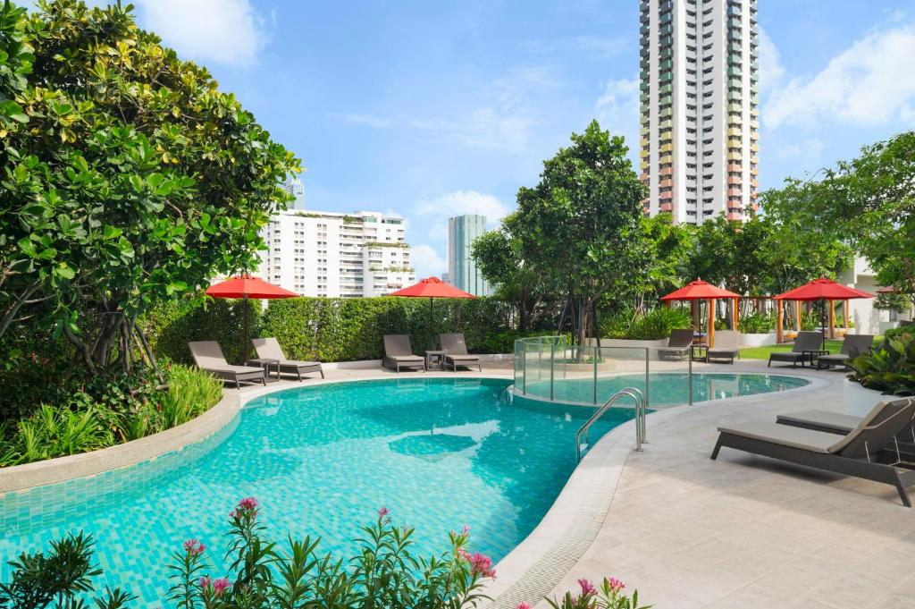 A landscaped outdoor pool deck with loungers, red umbrellas and high-rise surroundings.