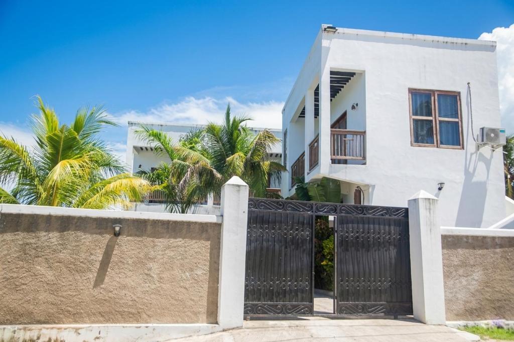 a white house with a black gate and palm trees at Bustan Inn in Kilima Juu Pwani