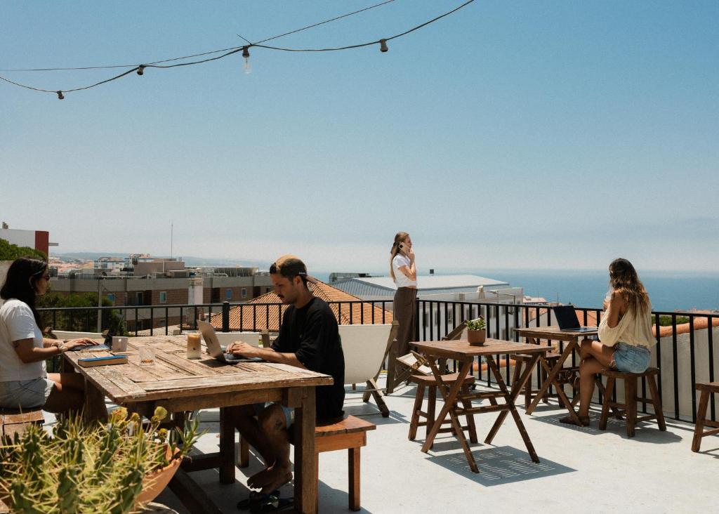 a group of people sitting at tables on a roof at Outsite Ericeira - Boavista in Ericeira