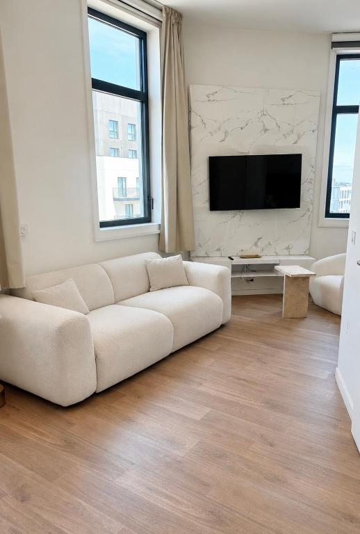 a white living room with a white couch and a tv at Mendess suites in Palaiseau