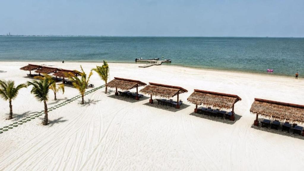 a beach with tables and palm trees and the ocean at La Maringa El Magnifico in Libreville
