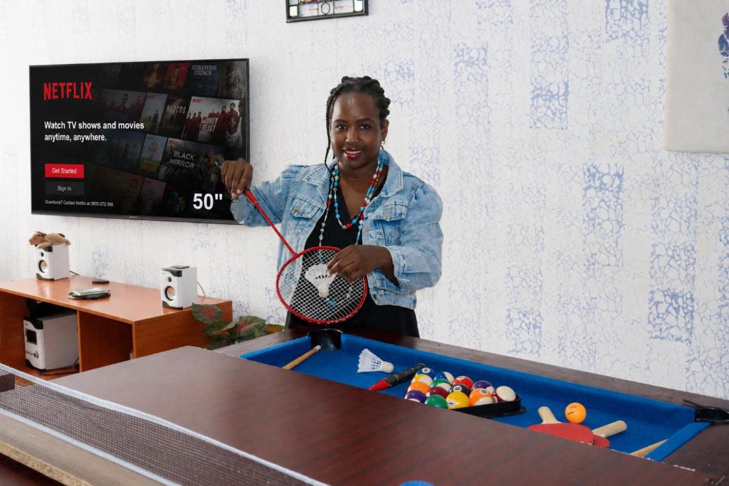 a woman holding a tennis racket in front of a table at Cozy Rooms JKIA -Games Nights - Gated - Secure -3 Bedroom -5 Beds -2Baths -15Mins to JKIA-SGR in Syokimau