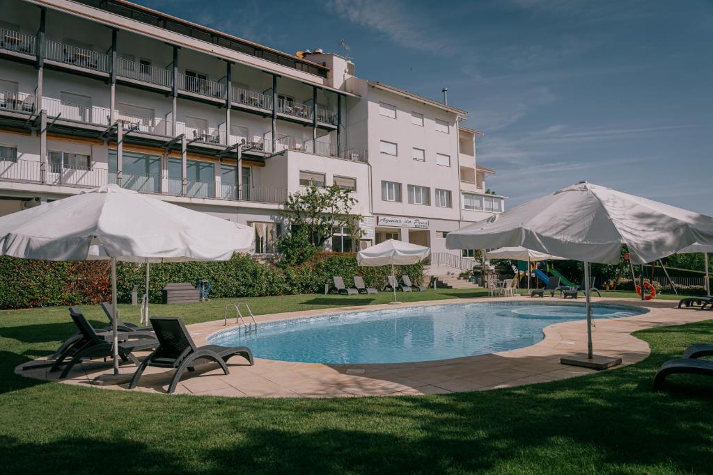 a swimming pool with umbrellas and chairs and a building at Hotel Aguiar da Pena in Vila Pouca de Aguiar
