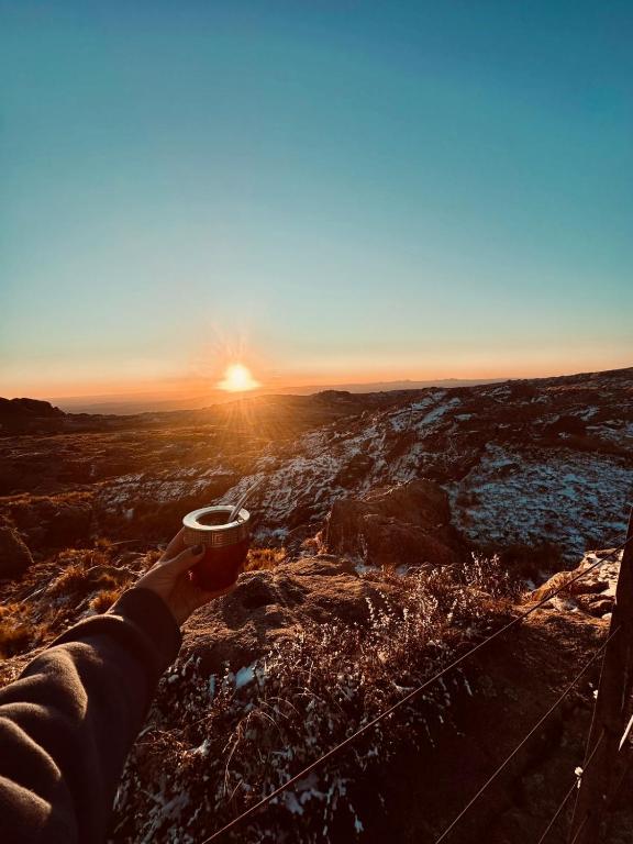 a person holding a cup of coffee as the sun sets at Rinconcito Serrano in Mina Clavero