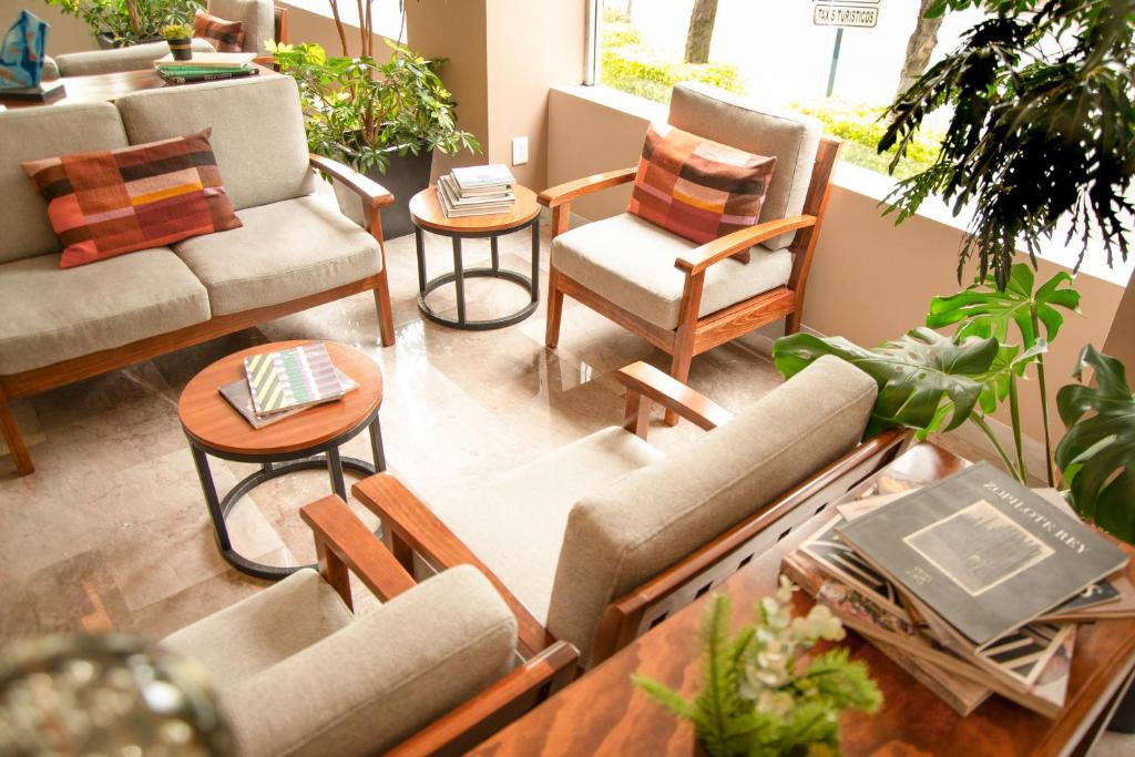 A bright window-side lobby lounge with sofas, armchairs, plants, and reading tables.