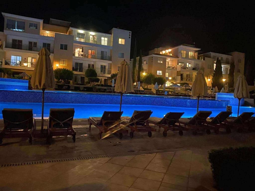 a group of chairs and umbrellas next to a pool at night at Elysia park wellness 2 bedroom apartment in Paphos