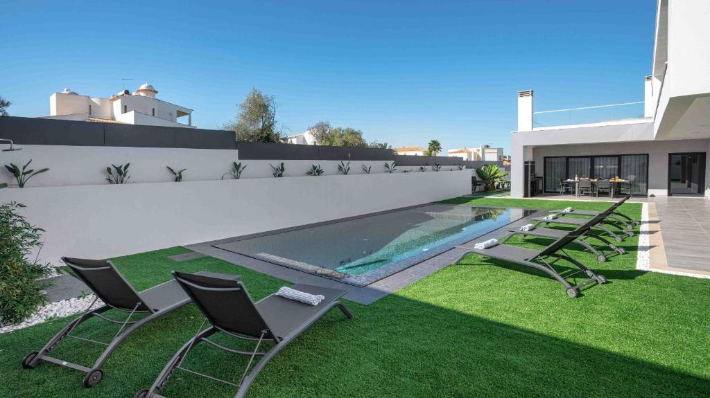 a backyard with a swimming pool and chairs on the grass at Private Alvor villa with pool and Jacuzzi in Alvor