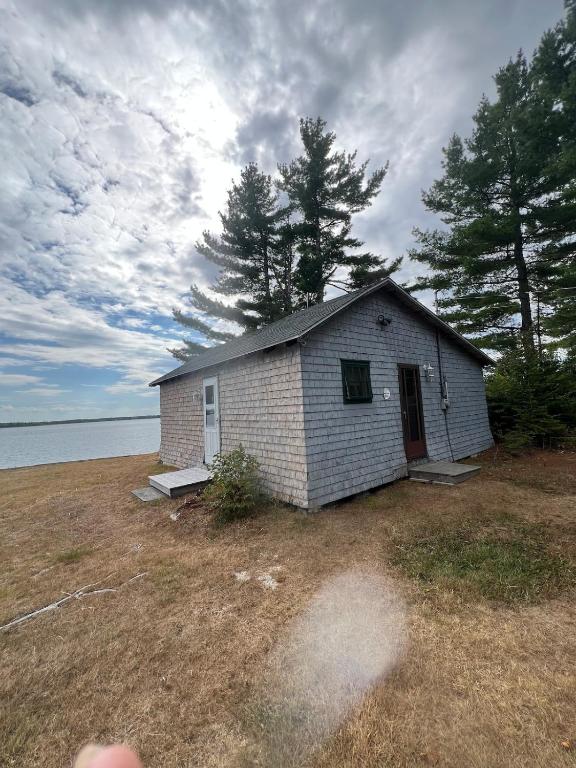 a small house in a field next to the water at Bob's Cabin at Wishart's Point Lodge in Neguac