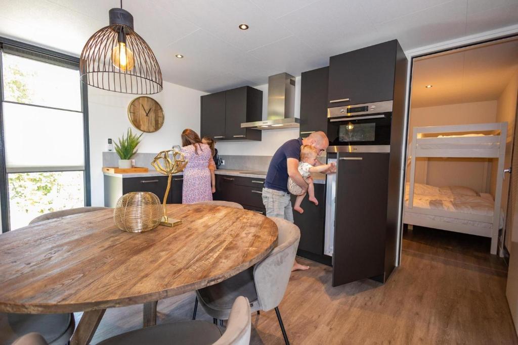 a man holding a baby in a kitchen with a table at Forest Cube 5 persons #702 in Maasbree