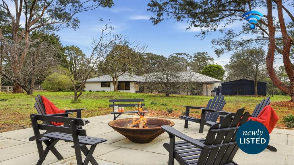 a fire pit in a yard with three chairs at Mirambeena in Berrima