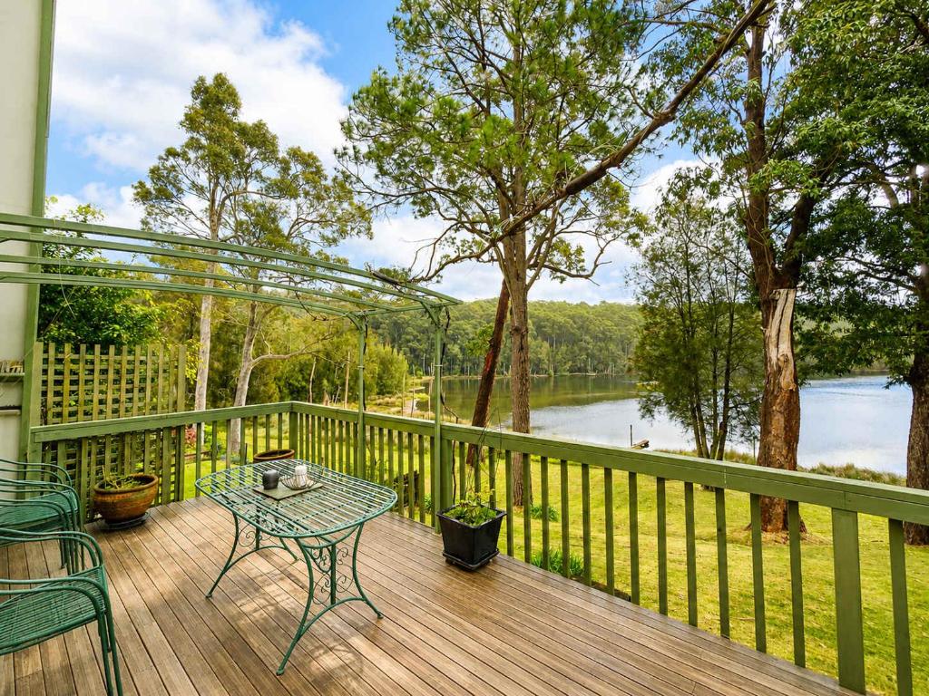 a table and chairs on a deck with a view of a lake at Cottage on the Lake - peaceful Burrill Lake escape in Burrill Lake