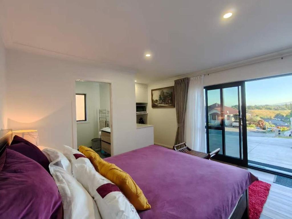 a bedroom with a purple bed and a large window at Private Cozy Sleepout with Free Parking & Self Check-in in Hamilton