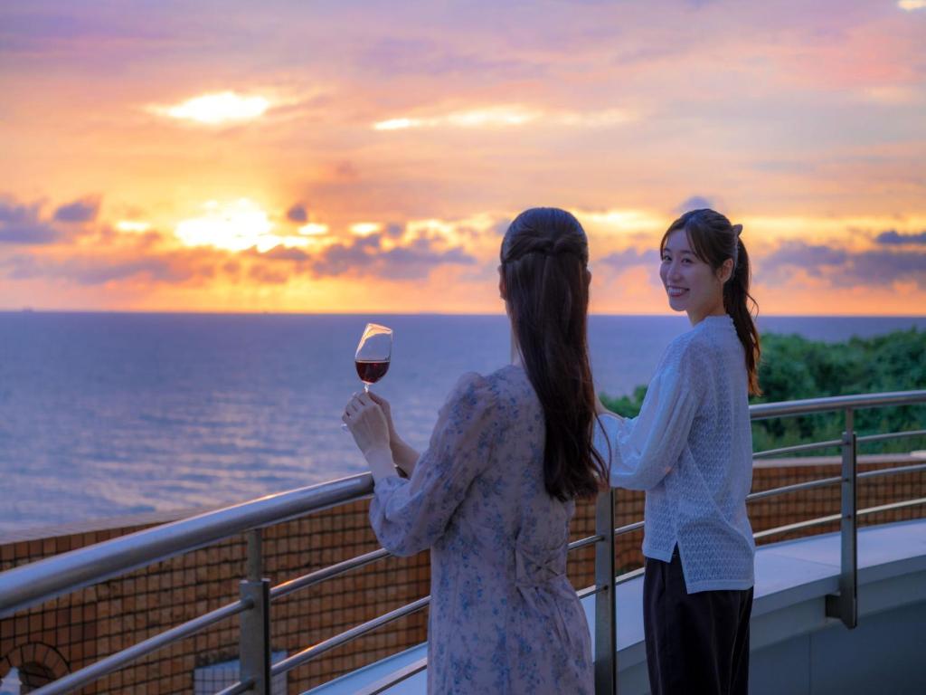 two women standing on a balcony holding a glass of wine at KAMENOI HOTEL Genkainada All-Inclusive Resort in Kitakyushu
