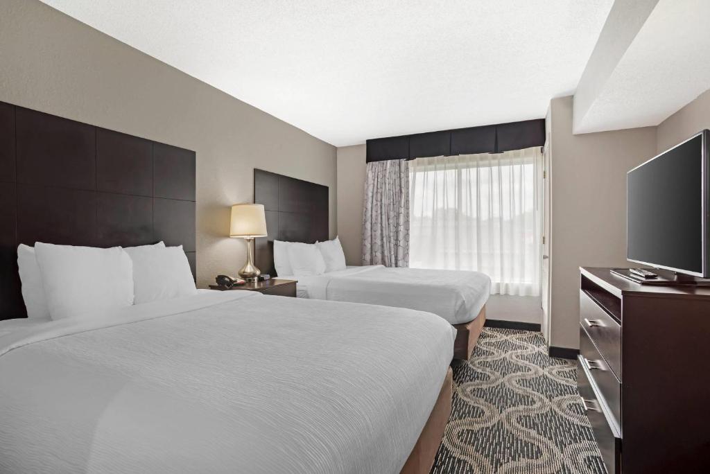 a hotel room with two beds and a flat screen tv at Quality Suites Pineville - Charlotte in Charlotte