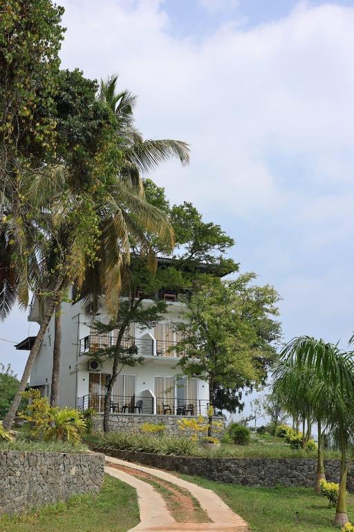 a white house with palm trees and a dirt road at FlyOn Resort in Dickwella