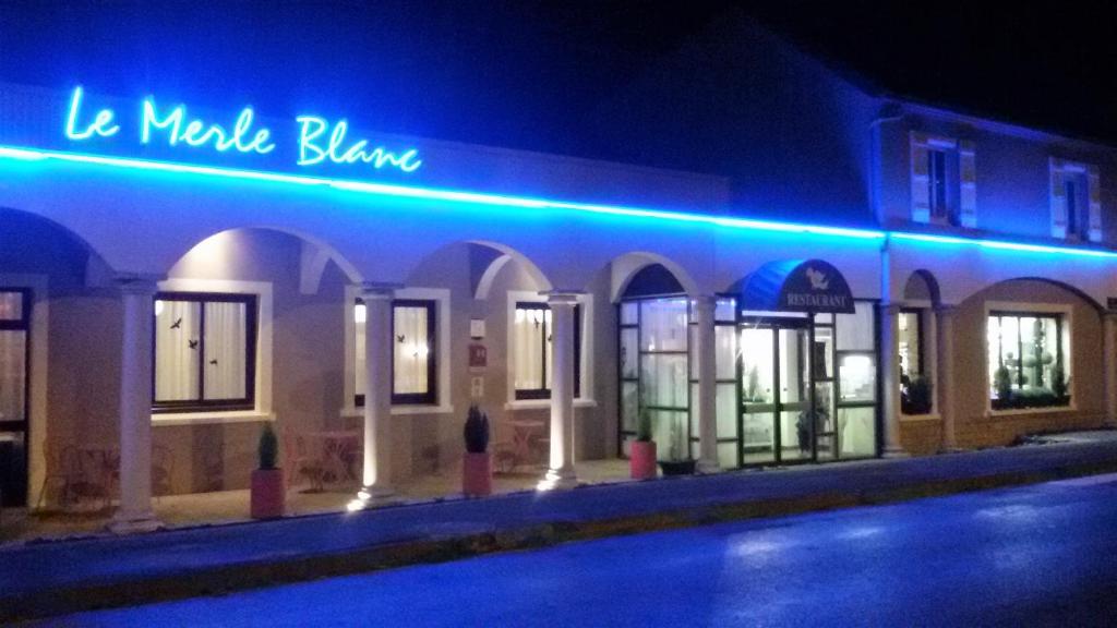 ディゴワンにあるLe Merle Blanc Hôtel Logisの青いネオンの看板が貼られた建物