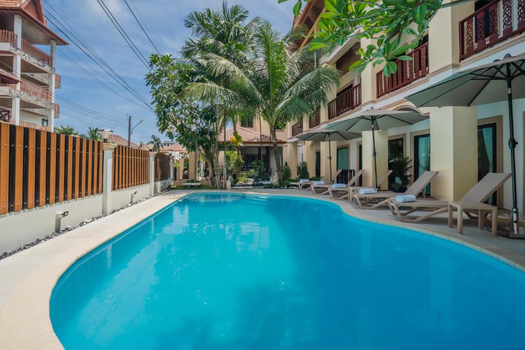 a swimming pool at a hotel with chairs and palm trees at Westkey Patong Hotel in Patong Beach
