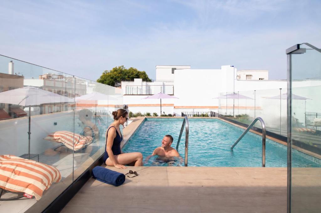 two women sitting next to a swimming pool at Líbere Seville Triana in Seville