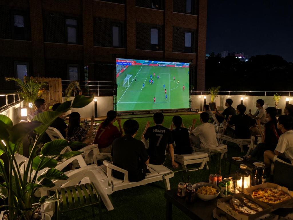 a group of people sitting in chairs watching a video game at Bluedot Poshtel in Seoul