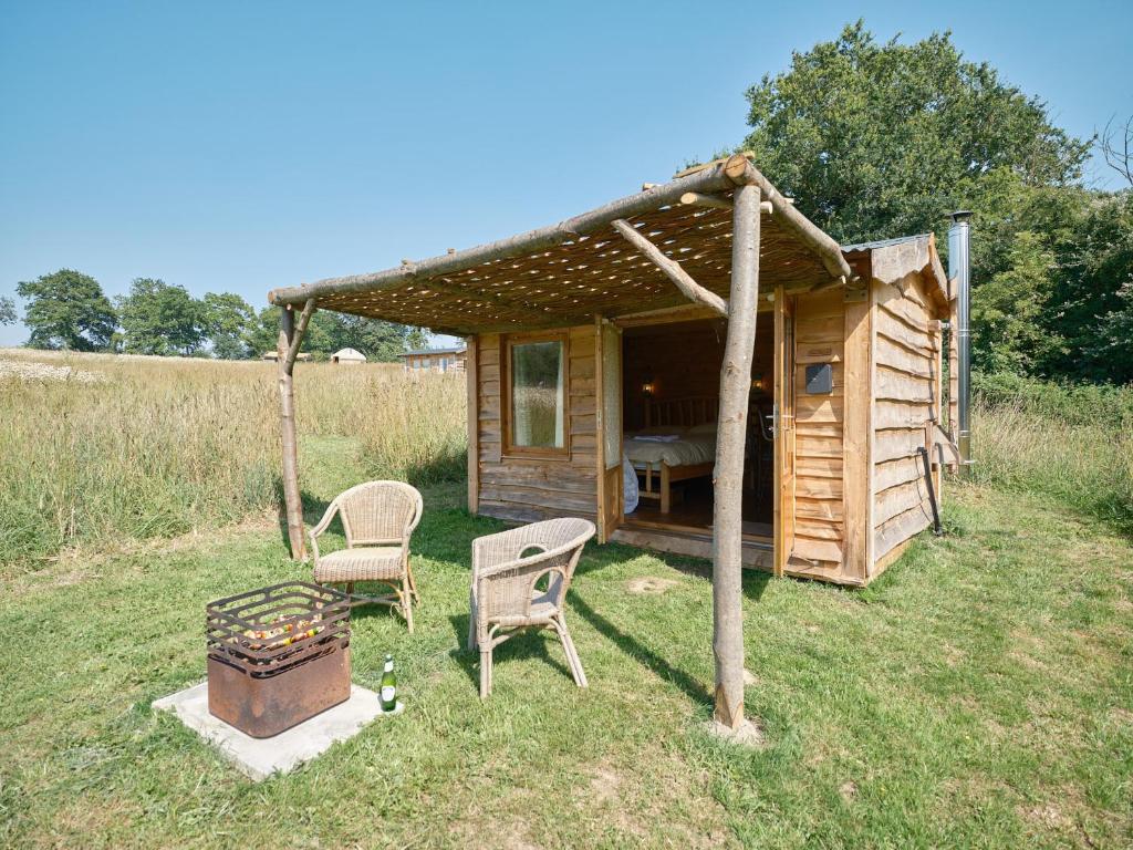 a cabin with two chairs and a grill in the grass at Simple Basketmakers Hut Cabin for Two in Chiddingstone