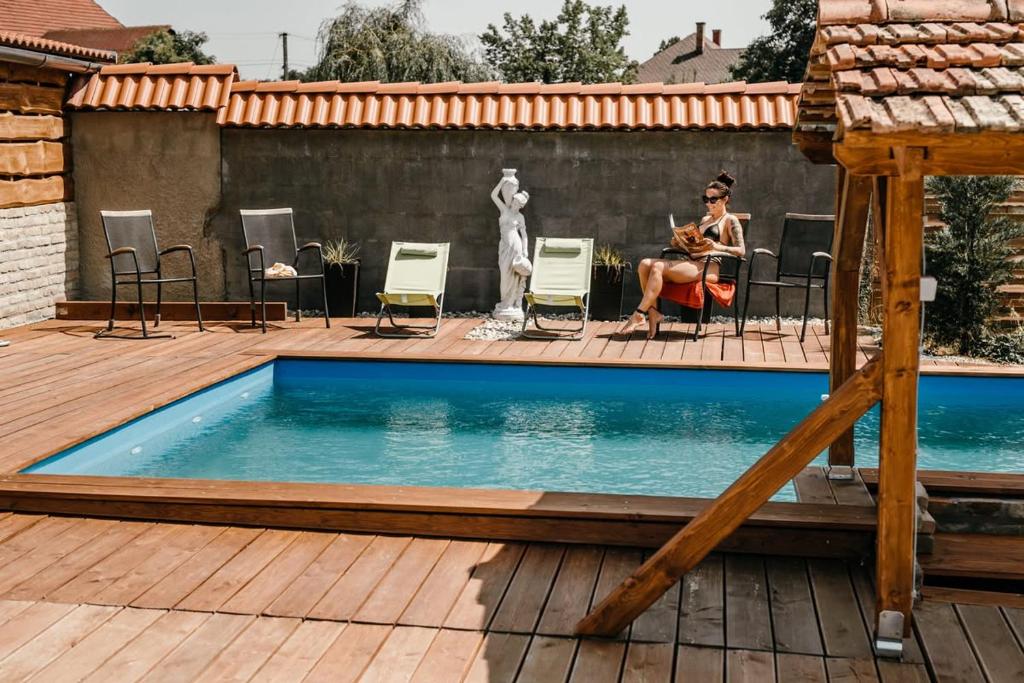 a woman sitting on a deck next to a swimming pool at Harmónia Aqua Vendégház in Somogysárd