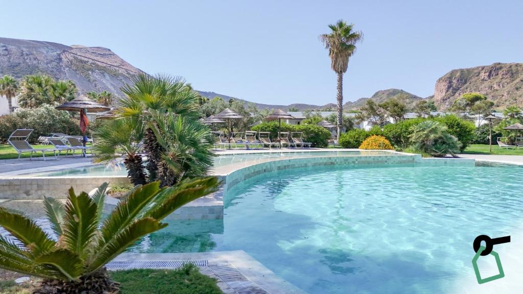 a swimming pool with palm trees and mountains in the background at Hotiday Vulcano Porto in Vulcano