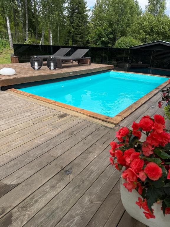a swimming pool with a wooden deck and red flowers at Villa Ensola with pool in Savonlinna