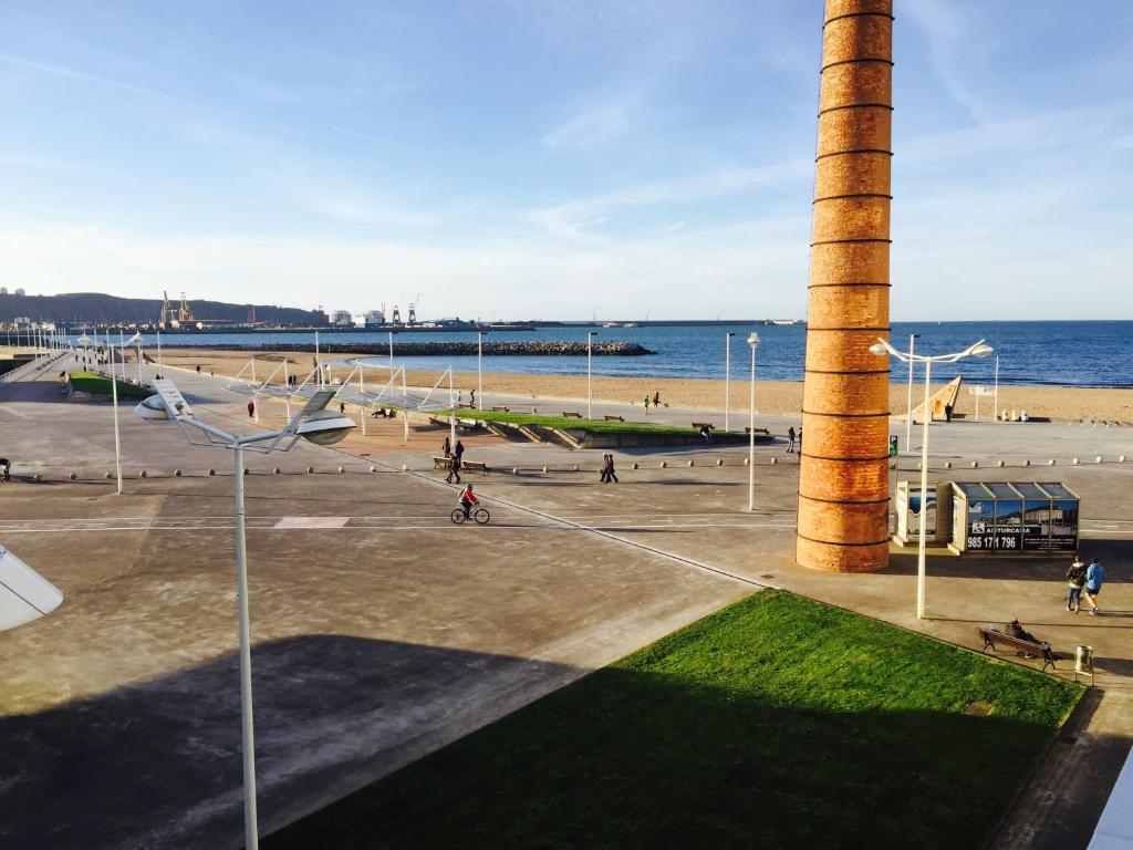 Blick auf einen Strand mit einem Leuchtturm und das Meer in der Unterkunft Apartamento Playa Poniente in Gijón