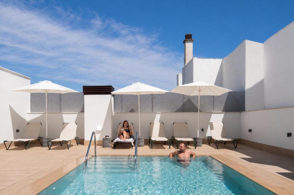 a man and a woman sitting in a swimming pool at Líbere Seville Plaza Nueva in Seville