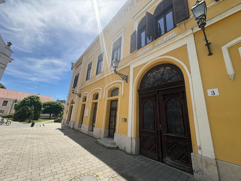 a yellow building with a black door on a street at Campana Apartment - Szigetvár in Szigetvár