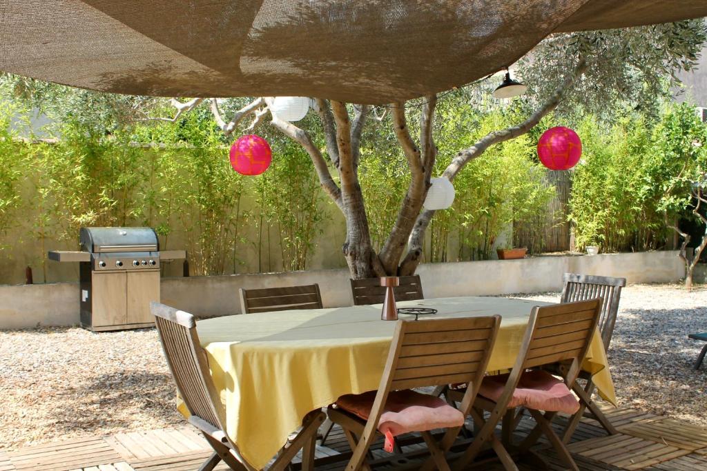 a table with a yellow tablecloth and chairs under a tree at RDC dans maison "ilolil" a 1km plage de la Coudoulière in Six-Fours-les-Plages