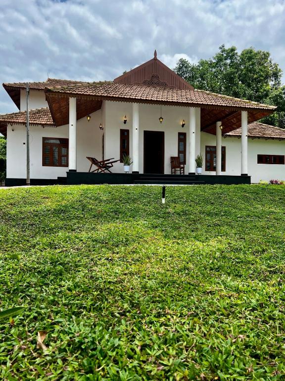 a small white house with a grass field in front of it at Haritham Heritage Villa in Vadakkāncheri