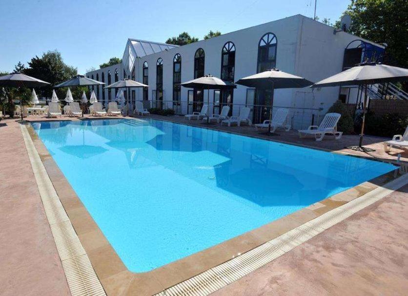 a large blue swimming pool with chairs and umbrellas at Agape Hotel Niort- Bessines in Bessines