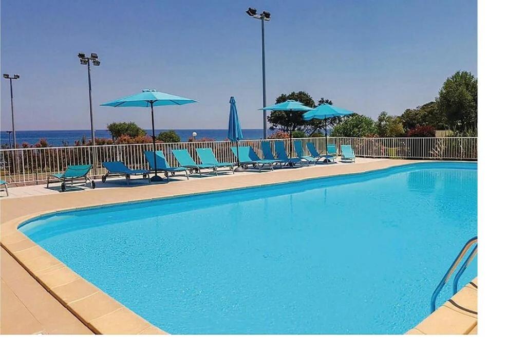 a swimming pool with blue chairs and umbrellas at Studio vue mer in Cervione