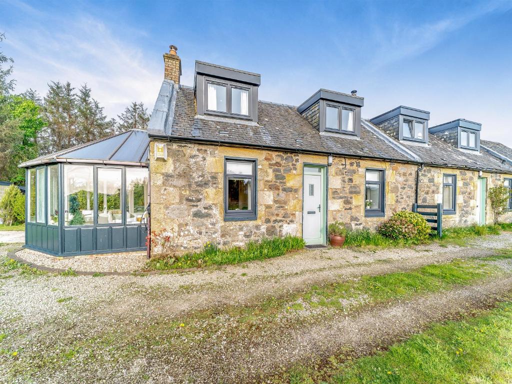 an old stone house with a greenhouse in front of it at Torr Cottage in Dalrymple