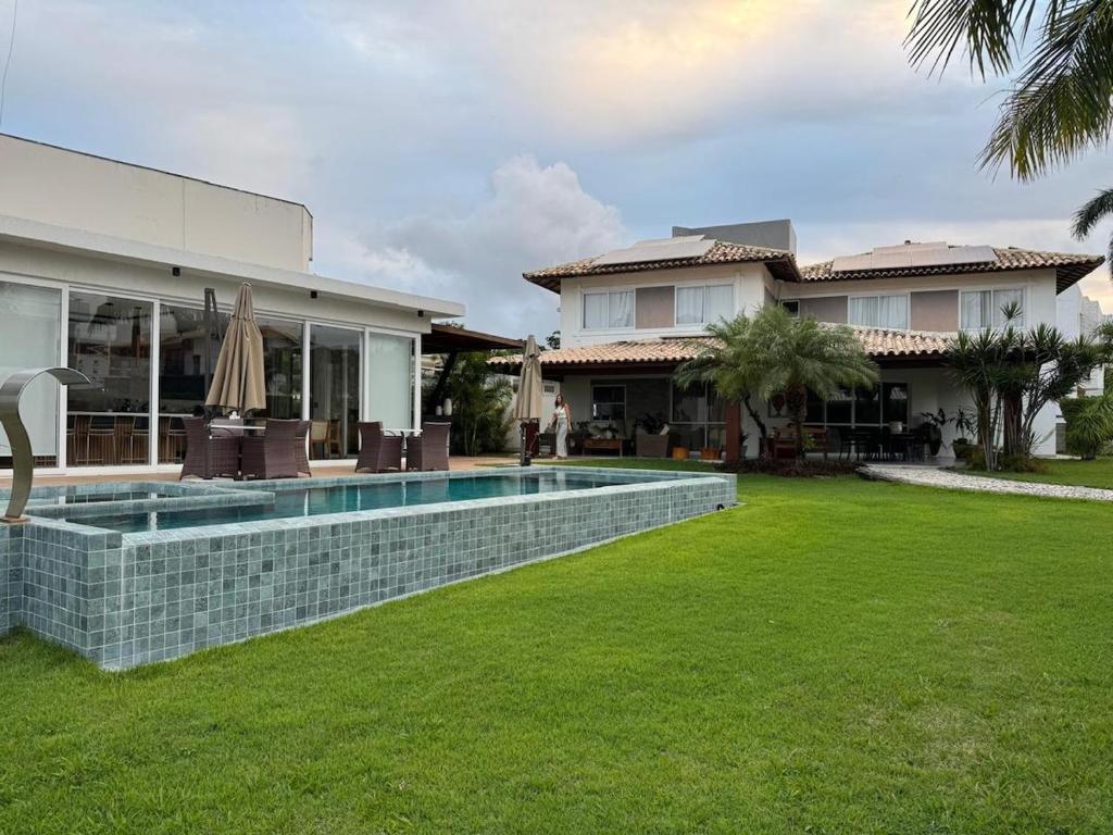 a house with a swimming pool in front of a yard at Guarajuba com 5 suítes, piscina e espaço gourmet in Camacari