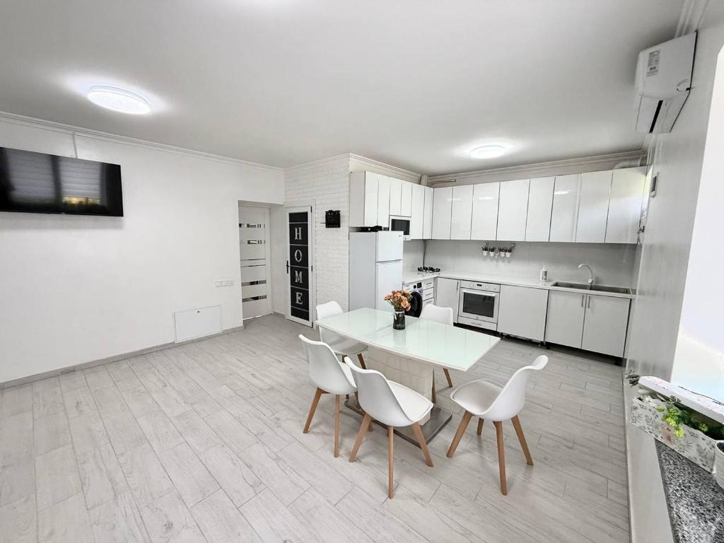 a white kitchen with a table and white chairs at Apartment HOME две спальни in Reni