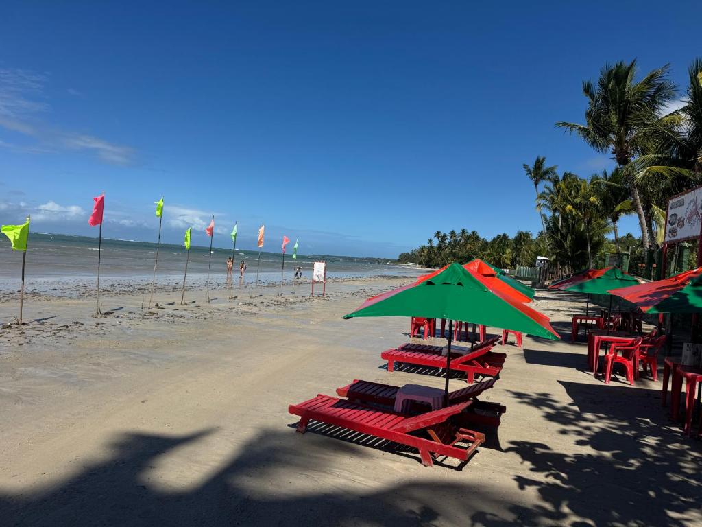 a beach with red chairs and green umbrellas at Pousada Caranguejo in Cairu