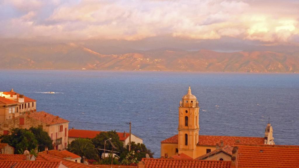 ein Gebäude mit einem Uhrturm direkt am Meer in der Unterkunft Solacargese-Le Jardin d'Irène-Vue panoramique exceptionnelle sur la Méditerranée in Cargèse