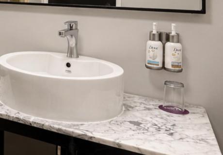 A vessel sink on a marble-look bathroom counter with wall-mounted toiletries.