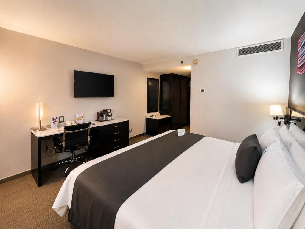A modern guest room with a king bed, desk, TV and beverage station.