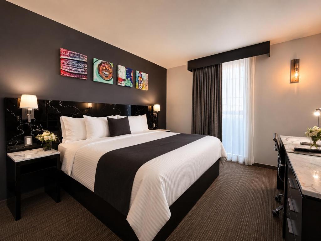 A dark-accented guest room with a large bed, window, desk and artwork.