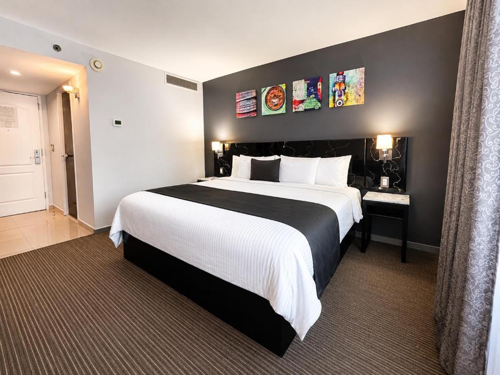 A spacious-looking guest room showing the bed, entry door, desk and curtained window.