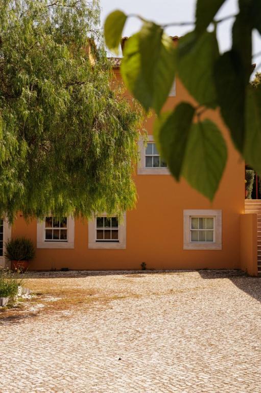 an orange house with white windows and a tree at Quinta De Catralvos in Azeitao
