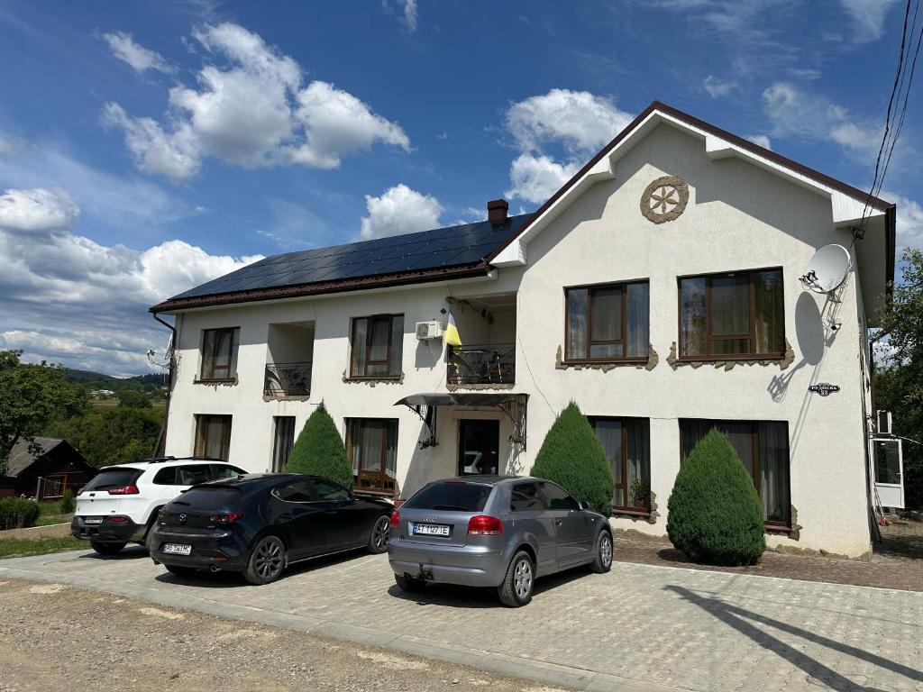 two cars parked in front of a white house at Hotel Dudarik in Kosiv